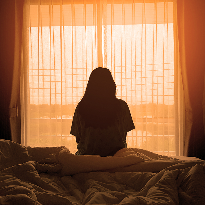 silhouette of woman sitting on the bed beside the windows with sunlight in the morning